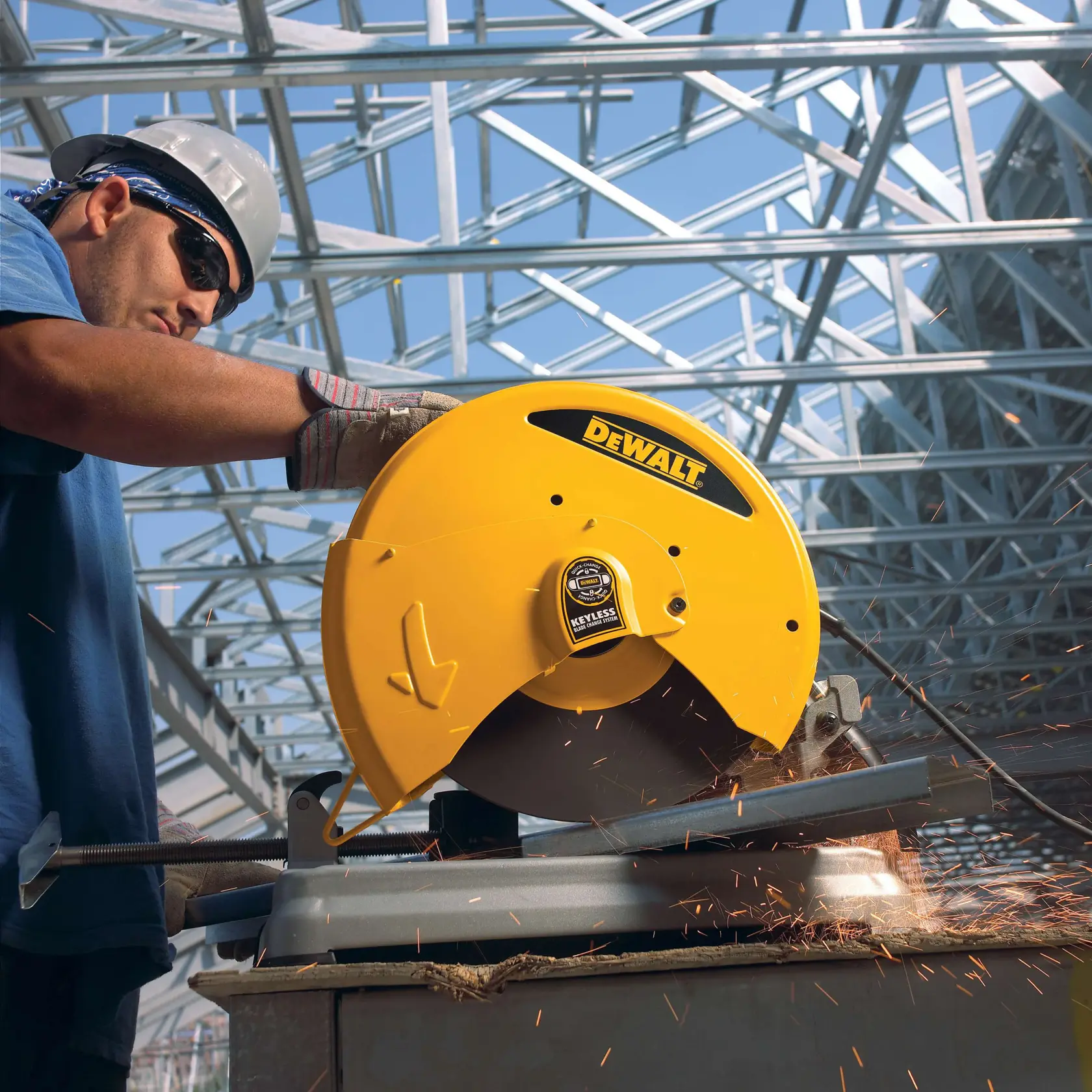 A worker using a DEWALT D28715 yellow metal cutting saw to cut a metal bar, with sparks flying. The scene takes place at a construction site with steel beams in the background.