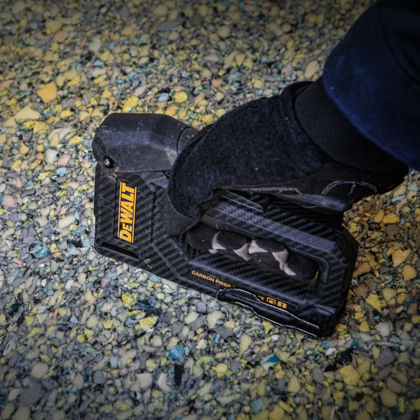 A person uses a DEWALT hand stapler to attach a sheet of material to a wooden frame at a construction site outdoors.